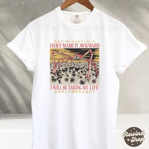 May include: White t-shirt with a graphic design featuring a red and yellow spider-like creature with multiple eyes. The text "I HAVE MADE IT AWKWARD" and "I WILL BE TAKING MY LIFE" are printed above and below the graphic, respectively.
