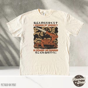 May include: Ivory-colored t-shirt with a graphic design featuring a crab holding a knife, with the text "I Abandon My Humanity" and "In Exchange For Crabhood". The shirt has a crew neck and short sleeves.