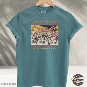 May include: Teal-colored t-shirt with a graphic illustration of a spider-like creature with red legs and a yellow body, surrounded by eyeballs. The shirt has Japanese text and the phrases "I HAVE MADE IT AWKWARD" and "I WILL BE TAKING MY LIFE".