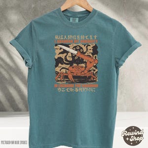 May include: Teal-colored t-shirt with a graphic featuring a crab holding a knife, an octopus, and text in English and Japanese. The text reads "I abandon my humanity" and "In exchange for crabhood".