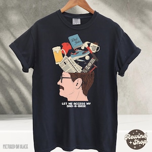 May include: Black t-shirt with a graphic of a man's head, open to reveal various items like a beer mug, sneakers, and a remote control. The text "LET ME ACCESS MY DAD-A-BASE" is below the head.