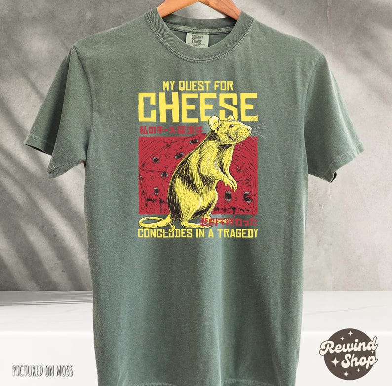 Op de afbeelding: Een groen T-shirt met een afbeelding van een rat en de tekst "My Quest for Cheese Concludes in a Tragedy".
