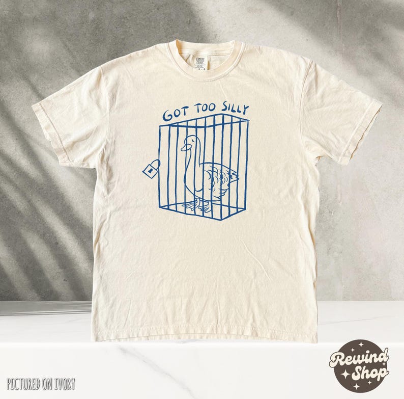 May include: A white t-shirt with a blue graphic of a goose in a cage. The text "Got Too Silly" is above the graphic.