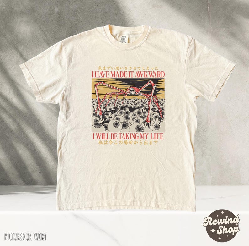 May include: Ivory-colored t-shirt featuring a graphic with a red and black spider-like creature over a field of eyeballs. The text reads "I HAVE MADE IT AWKWARD" and "I WILL BE TAKING MY LIFE" in English and Japanese.