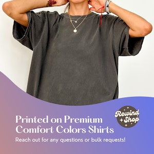 May include: A charcoal gray oversized t-shirt with a crew neck. The t-shirt is made of a soft, comfortable fabric. "Rewind Shop" is printed in a circle on the bottom right corner of the image.