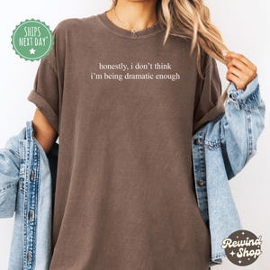 May include: A brown t-shirt with the text "honestly, i don't think i'm being dramatic enough" printed in white.