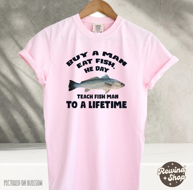 May include: Pink t-shirt with a graphic design that says "Buy a man eat fish, he day teach fish man to a lifetime". The graphic also includes a drawing of a fish.