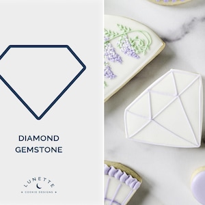 Puede incluir: Un cortador de galletas en forma de diamante y galletas decoradas. El cortador de galletas es un contorno azul oscuro de una forma de diamante. Las galletas son blancas con diseños florales morados y verdes y una forma de diamante.