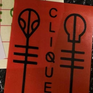 Pode incluir: Adesivo vermelho com a palavra "CLIQUE" em branco e dois s&iacute;mbolos pretos. Um adesivo branco com um s&iacute;mbolo preto tamb&eacute;m &eacute; vis&iacute;vel. Os adesivos est&atilde;o em uma superf&iacute;cie texturizada.