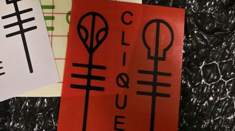 Pode incluir: Adesivo vermelho com a palavra "CLIQUE" em branco e dois s&iacute;mbolos pretos. Um adesivo branco com um s&iacute;mbolo preto tamb&eacute;m &eacute; vis&iacute;vel. Os adesivos est&atilde;o em uma superf&iacute;cie texturizada.