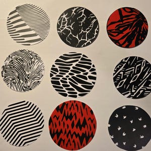 Op de afbeelding: Negen cirkelvormige ontwerpen met diverse zwart-witte patronen en twee rood-zwarte ontwerpen. De patronen omvatten zebra strepen, organische vormen en geometrische lijnen. De cirkels zijn gerangschikt in een raster van drie bij drie.