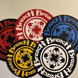 May include: A collection of round stickers with the word "Breach" in a stylized font. Each sticker features a central floral design and is colored in red, white, black, blue, and yellow.