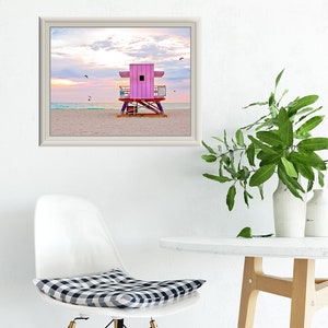 a chair and table with a framed pink lifeguard tower print above it.