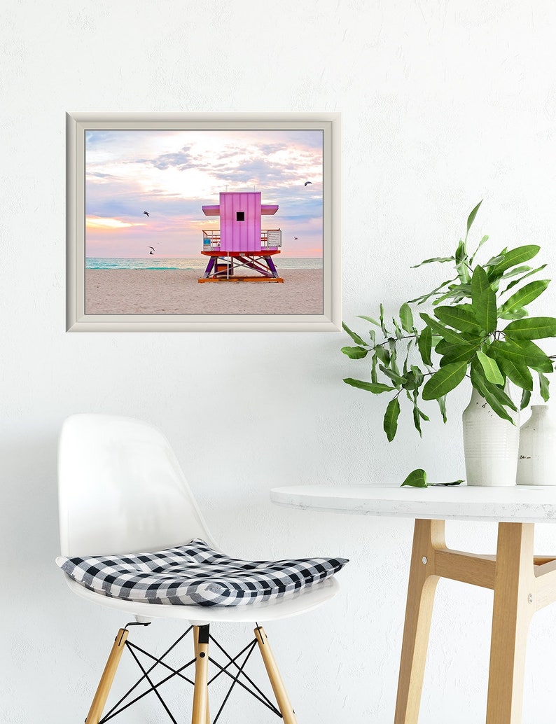 a chair and table with a framed pink lifeguard tower print above it.