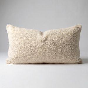 Puede incluir: Una almohada rectangular de color crema con una superficie texturizada y afelpada. La almohada tiene una apariencia suave y acogedora, perfecta para agregar comodidad y estilo a cualquier espacio habitable o dormitorio. El color neutro la hace versátil.