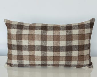 May include: A rectangular throw pillow featuring a woven plaid pattern in shades of dark brown, light brown, and cream. The fabric has a visible textured weave, and the pillow is shaped with straight edges and rounded corners in a standard rectangular form.