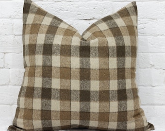 May include: A square throw pillow featuring a plaid pattern in shades of dark brown, medium brown, and cream. The fabric has a visible woven texture, and the pillow is plumped to create a soft, rounded shape with defined corners and edges.