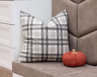 May include: A gray and white plaid pillow sits on a brown couch with a red fabric pumpkin in front of it.