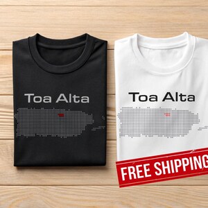 May include: Two t-shirts, one black and one white, with the text "Toa Alta" above a dotted outline of Puerto Rico. The black shirt has a grey outline with a red dot, while the white shirt has a grey outline.