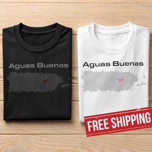 May include: Two t-shirts, one black and one white, featuring the text "Aguas Buenas" above a dotted outline of Puerto Rico. The Puerto Rico outline has a red dot. The white t-shirt has a red "FREE SHIPPING" stamp.