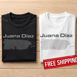 May include: Two t-shirts, one black and one white, each with the text "Juana Díaz" above a dotted outline of Puerto Rico. The black shirt has a red dot in the outline. The white shirt has a red dot in the outline.