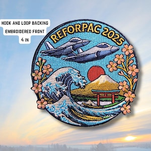 Może przedstawiać: Haftowana naszywka z motywem inspirowanym Japonią. Zawiera dwa myśliwce, falę, górę Fuji i kwiaty wiśni. Wyświetlany jest tekst "REFORPAC 2025". Średnica naszywki wynosi 10 cm.