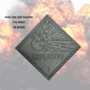 以下が含まれることがあります： 「EXPLOSIVE」の文字と数字の「1」がプリントされた、グレーのひし形のパッチ。パッチは3Dデザインで、「HOOK AND LOOP BACKING」と「PVC FRONT」の文字が特徴です。