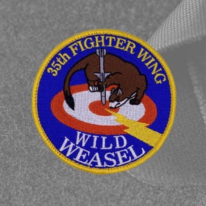 May include: A blue and yellow embroidered patch with a weasel attacking a target. The patch reads "35th Fighter Wing Wild Weasel".