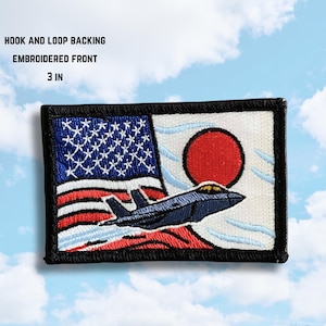 May include: Embroidered patch featuring the flags of the United States and Japan, with a dark blue jet aircraft. The patch is 7.6 cm in size and has hook and loop backing.