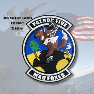 May include: A circular patch with a cartoon fox wielding a hammer, labeled "PATRON FIVE" and "MAD FOXES." The patch features a blue sky, yellow land, and palm trees. The text "HOOK AND LOOP BACKING," "PVC FRONT," and "3D DESIGN" are also visible.