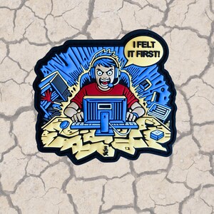 May include: A cartoon patch with a blue and yellow background. A person with blue hair is sitting in front of a computer with a headset on. The person is yelling "I felt it first!" in a speech bubble.