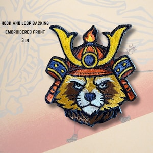 May include: Embroidered patch featuring a raccoon wearing a samurai helmet. The patch is 3 inches in size and has a hook and loop backing. The design includes yellow, orange, blue, brown, and white colors.