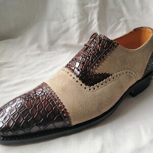 May include: Brown and beige leather dress shoes with a crocodile pattern on the toe and side. The shoes have a lace-up closure and a brogue design.