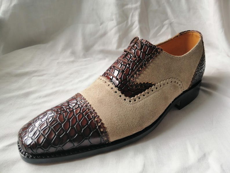 May include: Brown and beige leather dress shoes with a crocodile pattern on the toe and side. The shoes have a lace-up closure and a brogue design.