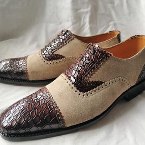 May include: A pair of brown and beige leather dress shoes with a crocodile pattern on the toe and sides. The shoes have a lace-up closure and a brogue design.