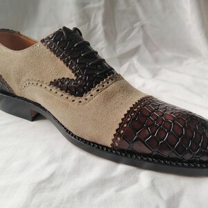 May include: A pair of brown and beige leather dress shoes with a brogue design. The shoes have a lace-up closure and a textured leather pattern on the toe.