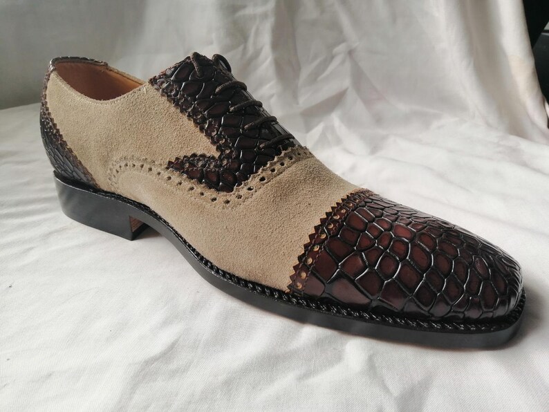 May include: A pair of brown and beige leather dress shoes with a brogue design. The shoes have a lace-up closure and a textured leather pattern on the toe.