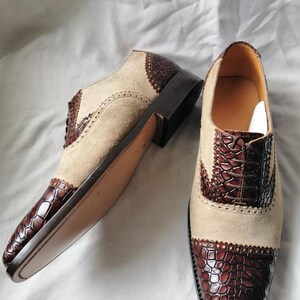 May include: A pair of brown and beige leather shoes with a crocodile pattern on the toe and heel. The shoes have a lace-up closure and a brogue design.