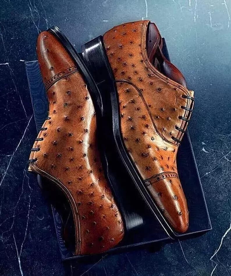 May include: A pair of brown leather oxfords with an ostrich skin pattern. The shoes have black laces and a black sole.