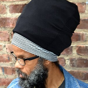 Puede incluir: Un hombre con un turbante negro y blanco con un patrón, una barba larga gris y gafas. Lleva una chaqueta vaquera.