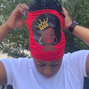 May include: A red headband featuring a black graphic of a woman with a crown, gold hoop earrings, and closed eyes. The headband is being worn by a person wearing a white t-shirt.