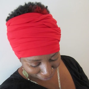 Peut inclure: Un turban rouge en tissu. Le turban est porté par une personne à la peau foncée et aux cheveux courts et bouclés.