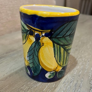 May include: A blue ceramic mug with a yellow rim and a painted design of lemons and green leaves.