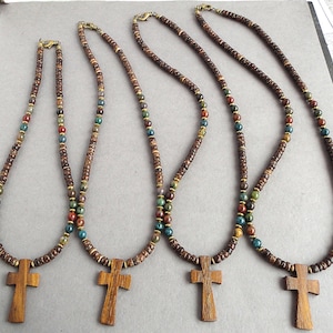 May include: Four wooden cross necklaces with brown, green, and red beads. The crosses are made of dark wood and have a simple design.