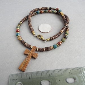 May include: A brown wooden cross pendant on a brown, blue, and red beaded necklace. The necklace is made of wood beads and has a brass clasp.