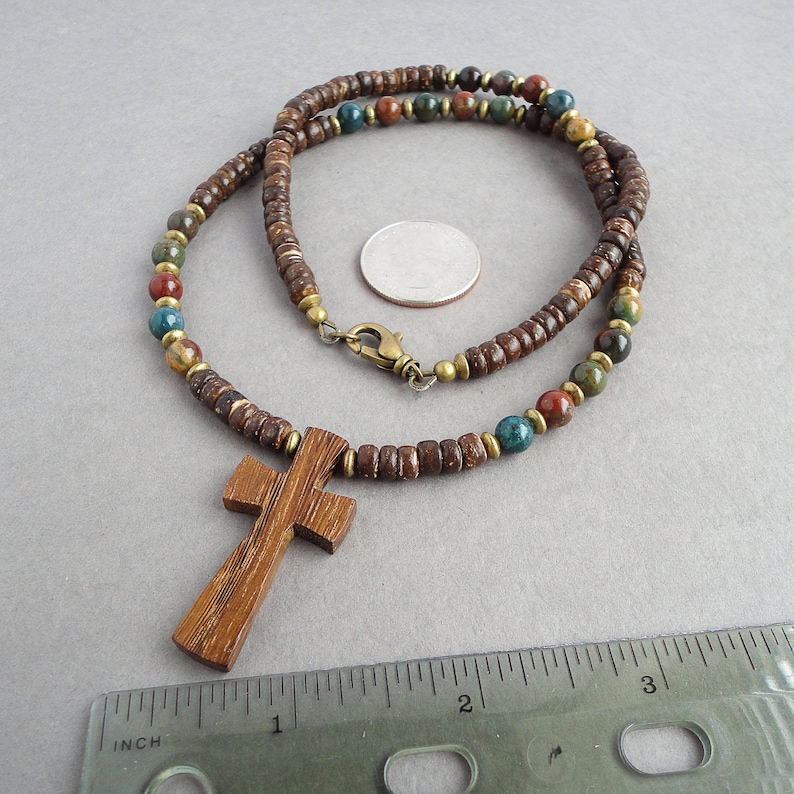 May include: A brown wooden cross pendant on a brown, blue, and red beaded necklace. The necklace is made of wood beads and has a brass clasp.