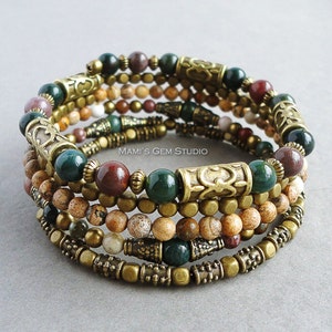 Pode incluir: Pulseira de várias voltas com contas de pedras preciosas verdes, marrons e bege, espaçadores de metal dourado e contas decorativas. "MAMI'S GEM STUDIO" está impresso na pulseira.