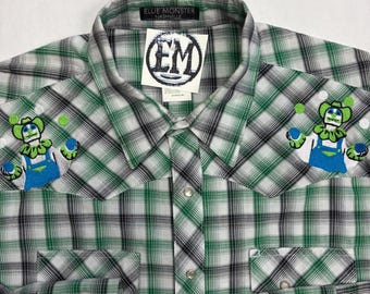 May include: A long-sleeve button-down shirt featuring a green, white, and black plaid pattern. The shirt has two chest pockets, silver-tone snap buttons, and embroidered patches of a clown juggling on each shoulder. A tag reads Ellie Monster.