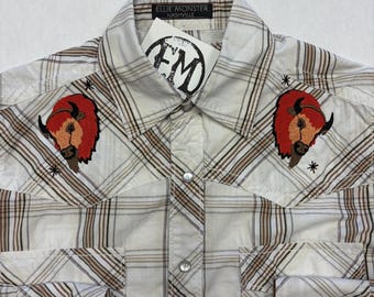 May include: Cream-coloured plaid shirt with brown stripes, featuring embroidered bison patches on the chest. The shirt has two front pockets and snap closures. The label reads "ELLIE MONSTER NASHVILLE".