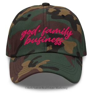 May include: Camouflage baseball cap with the embroidered text "god·family·business" in bright pink. The cap has a curved peak and a black button. The background is a classic green, brown, and black camouflage pattern.
